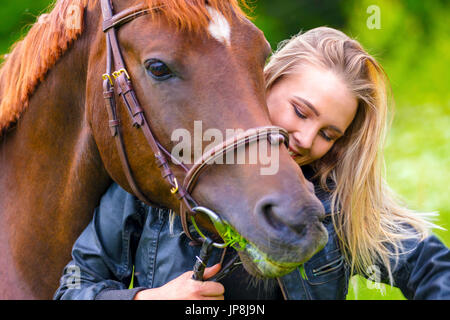 Belle femme nourrir son cheval arabe avec l'herbe dans le domaine Banque D'Images