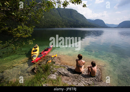 La mère et le fils assis dans l'eau peu profonde par leurs kayaks. Lac de Bohinj, en Slovénie. Banque D'Images