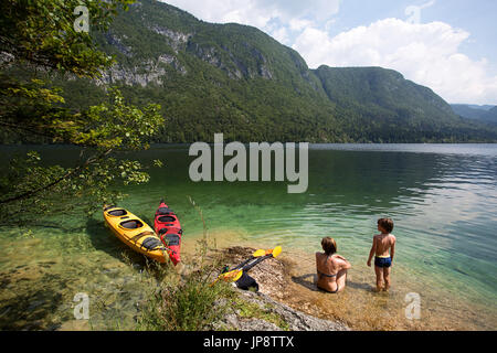 La mère et le fils assis dans l'eau peu profonde par leurs kayaks. Lac de Bohinj, en Slovénie. Banque D'Images