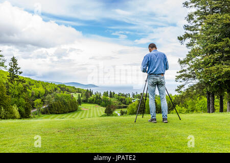 Vue paysage vert de golf avec des collines en été à La Malbaie, Québec, Canada dans la région de Charlevoix avec la photographe et trépied Banque D'Images