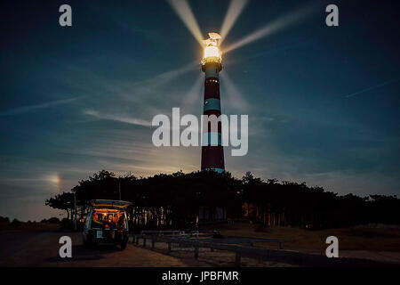 Une voiture devant le phare sur l'île Ameland par nuit, la lune se lève derrière la forêt Banque D'Images