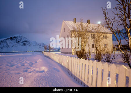 Pleine lune et lumières sur la maison en bois typique entouré de neige Flakstad Lofoten, Norvège du Nord Europe Banque D'Images