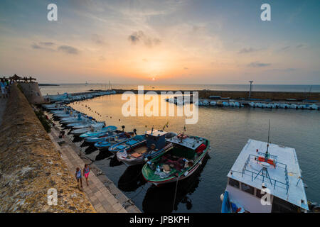 Des feux au coucher du soleil sur des bateaux amarrés dans le port entouré de murs médiévaux Gallipoli province de Lecce Pouilles Italie Europe Banque D'Images