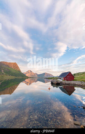 Soleil de minuit sur peaks et typique rorbu reflétée dans la mer claire de nuit Vengeren Vagpollen Lofoten, Norvège Europe Banque D'Images