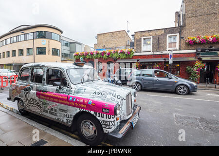 Taxi couvert d'autocollants publicitaires dans les rues commerçantes de Camden Market North West London United Kingdom Banque D'Images