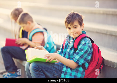 Les enfants avec des sacs à dos assis sur l'escalier près de l'école Banque D'Images