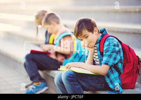 Les enfants avec des sacs à dos assis sur l'escalier près de l'école Banque D'Images