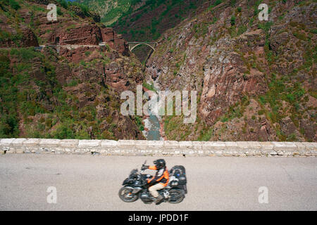 Motocycliste (avec flou de mouvement) sur une route à flanc de falaise au-dessus de la rivière Var, pont de la mariée au loin. Guillaumes, gorge de Daluis, France. Banque D'Images
