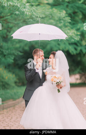 Le portrait de l'émotionnel cheerful newlyweds marcher sous le parapluie dans le parc au printemps. Banque D'Images