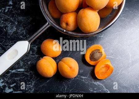 Organique mûres les abricots dans une passoire en acier. Composition dans un style rustique - jaune bio abricots juteux dans son ensemble et passoire en acier et des moitiés d'abricots o Banque D'Images