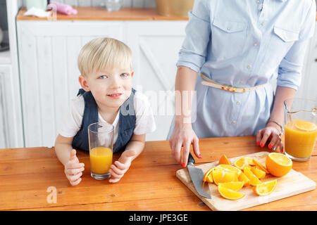 Maman coupe de fruits pour son fils. sliced oranges sur une planche à découper en bois. Petit-déjeuner sain et savoureux Banque D'Images