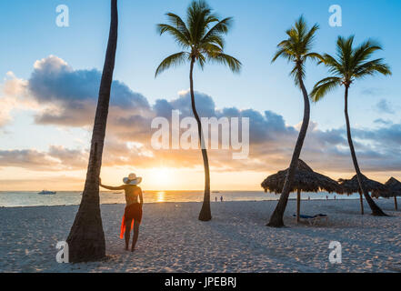 Bavaro Beach, Bavaro, Higuey, Punta Cana, République dominicaine. Woman admiring le lever du soleil sur une plage bordée de palmiers (MR). Banque D'Images