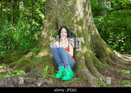 Femme assise sous les arbres matures à woodland Banque D'Images