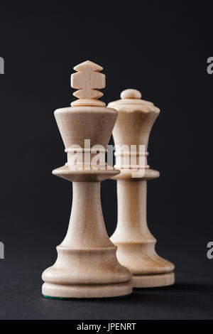 Pièces des échecs en bois, les figures du roi et de la reine blanche isolé sur fond de couleur noire. Banque D'Images
