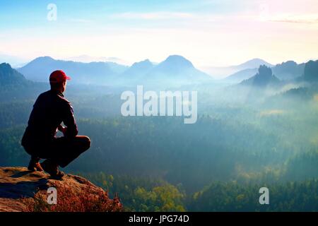 Coureur de tête rouge et sombre en position accroupie en vêtements sur un rocher, profiter du paysage Banque D'Images