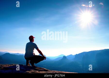 Coureur de tête rouge et sombre en position accroupie en vêtements sur un rocher dans la région de Heather buissons, profiter du paysage Banque D'Images