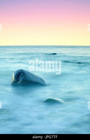 Atmosphère romantique dans la matinée en mer. Gros rochers qui sortent de la mer ondulée lisse. Horizon rose avec premier rayons de soleil chaud. Banque D'Images