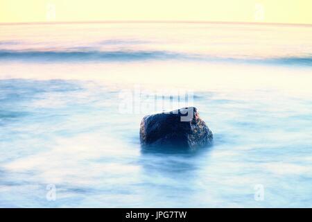 Atmosphère romantique dans la matinée en mer. Gros rochers qui sortent de la mer ondulée lisse. Horizon rose avec premier rayons de soleil chaud. Banque D'Images