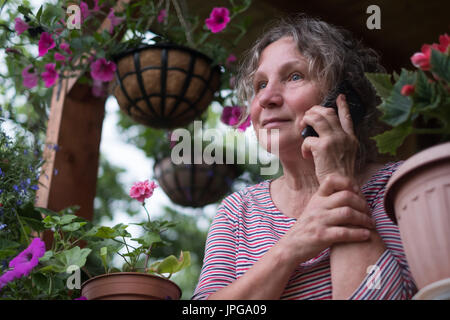 Mature femme appelant sur le téléphone et à la recherche sur les fleurs Banque D'Images