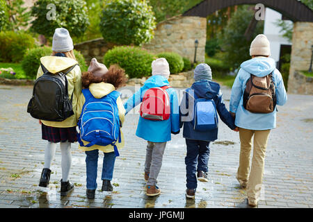 Schoolkids dans casualwear avec sacs à dos derrière dos holding par les mains tout en allant à l'école Banque D'Images