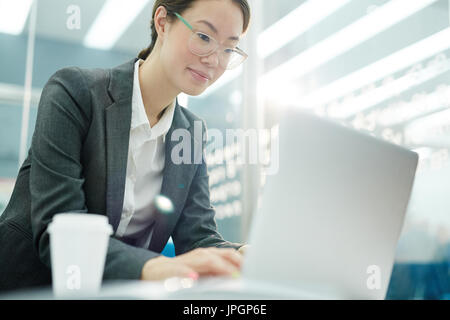 Portrait of young Asian businesswoman wearing glasses using laptop tout en travaillant dans un bureau moderne Banque D'Images