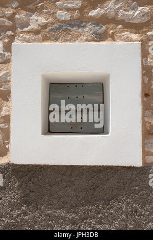 Très petite fenêtre carrée, peint en blanc, surround, de minuscules, de l'obturateur en bois bleu, avec des trous, Halki, Grèce Banque D'Images