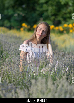 Belle femme en journée ensoleillée portant robe rose et assis dans le champ de lavande fraîche, appréciant la beauté de la nature Banque D'Images