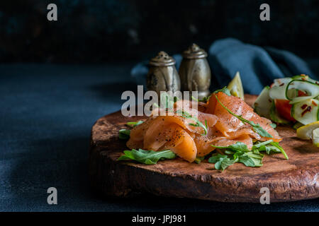 Saumon fumé avec salade de tomates et de concombre. Guéri, gravlax, saumon salé. Apéritif sur vintage wooden board, sur fond sombre, rustique Banque D'Images