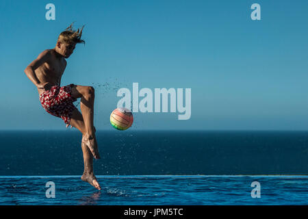 Un garçon passe à taper dans un ballon dans une piscine à débordement à l'été, jouer au football en vacances Banque D'Images