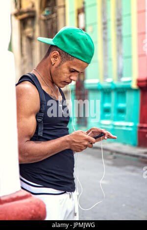 Un jeune homme utilise son appareil mobile avec des écouteurs sur les rues de la ville de La Havane, Cuba. Banque D'Images