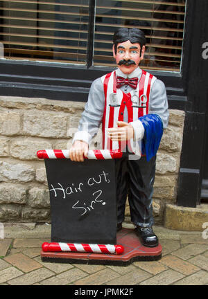 Signe unique, coloré et humoristique sur le sentier devant le salon de coiffure avec statue de barbier à l'ancienne demandant « A Hair cut Sir ? » Banque D'Images