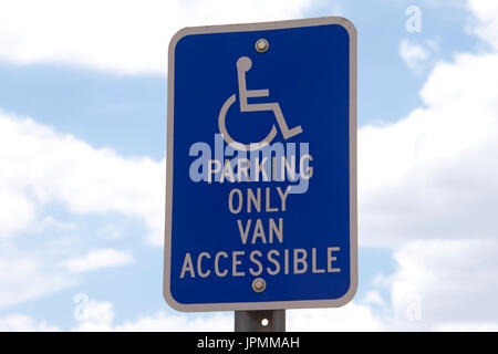 Handicap parking sign contre ciel bleu avec des nuages blancs moelleux en arrière-plan. Banque D'Images