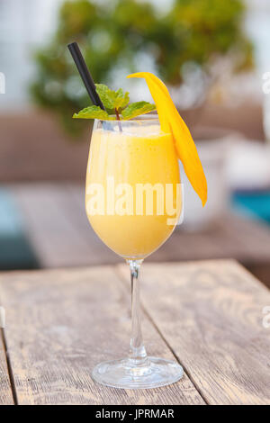 Smoothie mangue juteuse de en verre avec paille et décoration menthe sur table en bois. Jus sains. Banque D'Images