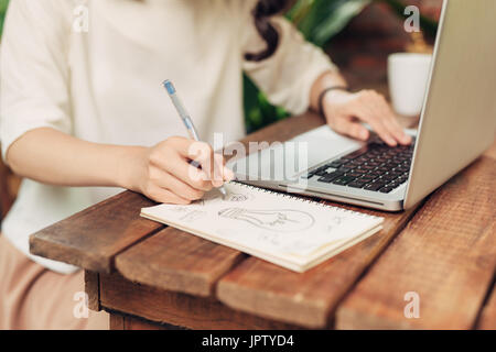 Young smiling woman sitting at table in cafe et écrit dans l'ordinateur portable Banque D'Images