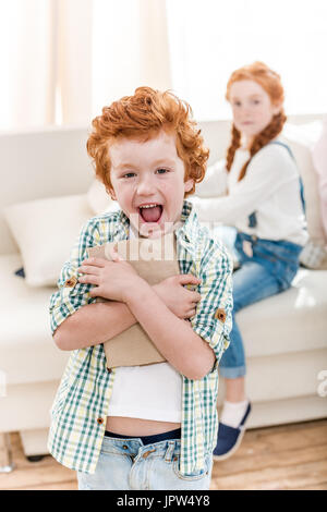 Petite fille assise sur le canapé et à la rousse à happy boy holding book, family fun at home concept Banque D'Images