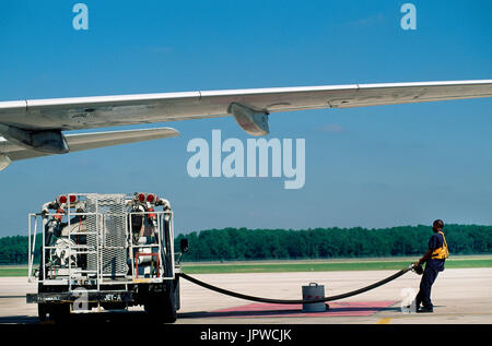 Jet-A1 bowser ravitaillement stationné sous un Airbus A320 aile gauche avec un ravitaillement en portant un haut jaune viz tabard tirant sur le tuyau de carburant Banque D'Images