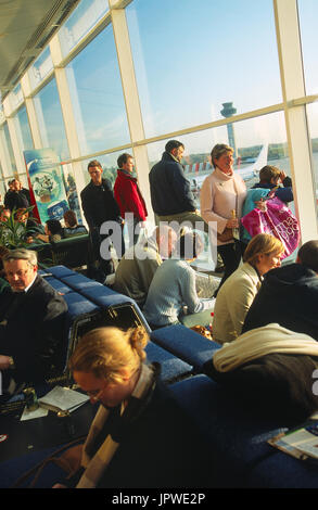 Les passagers qui attendent dans un salon bondé de départ porte à côté de windows à l'aide d'un contrôle du trafic aérien-tour et un Boeing 737-300 garée derrière Banque D'Images