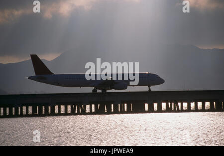 Airbus A321-100 taxiing générique à travers la voie de circulation du pont-jetée sur la mer avec les arbres de la lumière du soleil, soleil étincelant hors de l'eau et les nuages derrière Banque D'Images