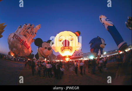 Foule de gens regardent comme des ballons à air chaud y compris clown, Mickey et Château Disney en forme spéciale gonflage des ballons dans une lueur de nuit à th Banque D'Images