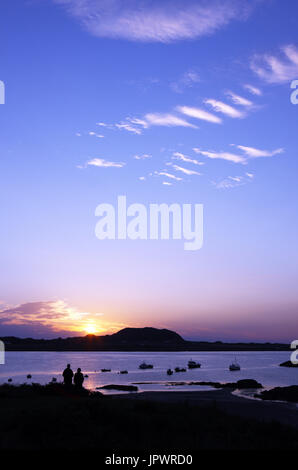 Couple regardant le coucher de soleil sur Iona de Fionnphort sur l'île de Mull, en Ecosse Banque D'Images