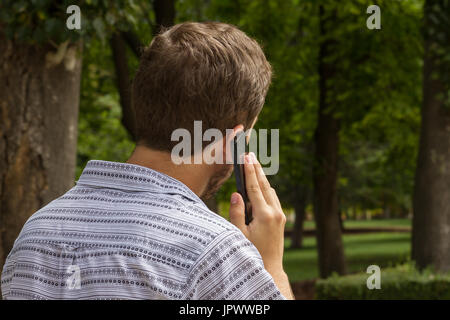 Vue arrière de casual man walking in park de Madrid et d'avoir une conversation téléphonique. Banque D'Images