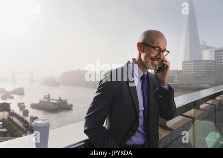 Businessman talking on cell phone on sunny, urban bridge, London, UK Banque D'Images