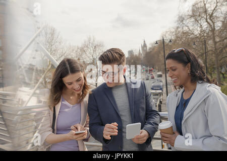 Des amis à l'aide de téléphones cellulaires et de boire du café sur urban bridge, London, UK Banque D'Images