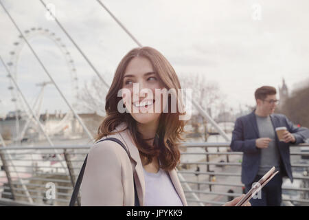 Smiling woman walking on urban bridge près de roue du millénaire, London, UK Banque D'Images