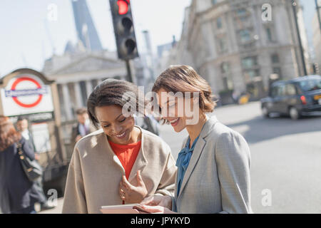 Smiling businesswomen with digital tablet on sunny urban city street Banque D'Images