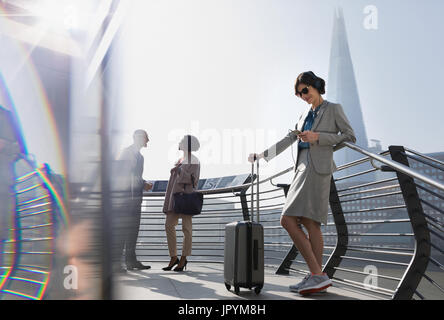 Businesswoman with suitcase écoutez de la musique avec des écouteurs et smart phone, London, UK Banque D'Images