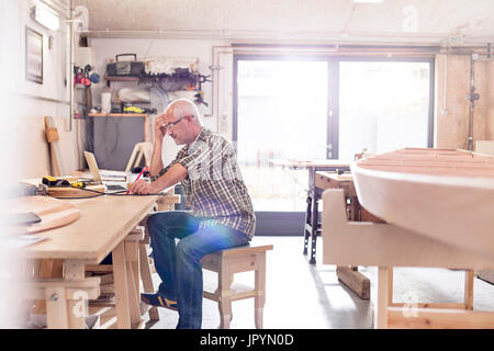 Male carpenter working at laptop sur l'établi près de bateau en bois dans l'atelier Banque D'Images