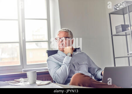 Confiant, pensive businessman with laptop sitting in office Banque D'Images