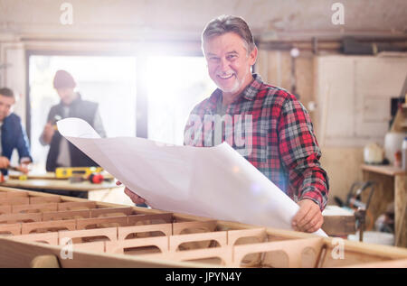 Portrait of smiling male carpenter de l'examen de plans au bateau en bois dans l'atelier Banque D'Images