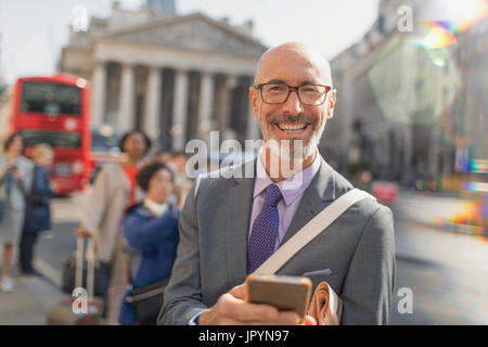 Portrait souriant, confiant businessman texting with cell phone on urban city Street, London, UK Banque D'Images